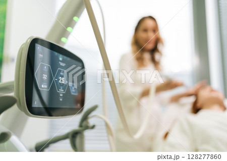 Remote view of blurred beautician performing mesotherapy treatment with specialized equipment, targeting wrinkle reduction and skin rejuvenation on female client face in modern aesthetic clinic Remote view of blurred beautician performing mesotherapy treatment with specialized equipment, targeting wrinkle reduction and skin rejuvenation on female client face in modern aesthetic clinic 128277860