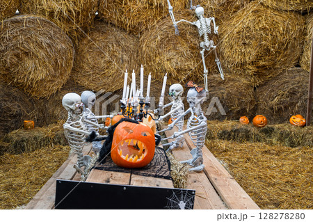 Halloween skeletons having dinner with pumpkins and candles on hay background Halloween skeletons having dinner with pumpkins and candles on hay background 128278280