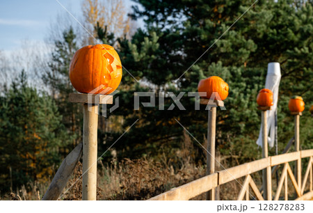 Carved Halloween pumpkins on wooden fence posts in autumn forest 128278283