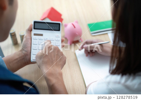 Couple Engaging in Financial Planning. Using calculator and piggy bank to strategize savings. 128278519