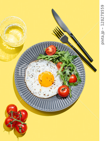 Fried eggs with arugula and cherry tomatoes on a dark plate on a bright yellow background Fried eggs with arugula and cherry tomatoes on a dark plate on a bright yellow background 128278559