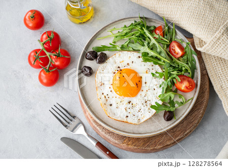 Fried eggs with arugula, ovives  and cherry tomatoes on a plate on a wooden board  128278564
