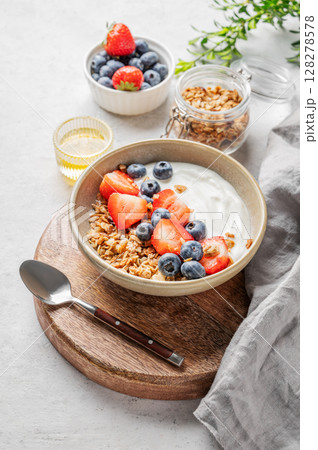 Natural yogurt with granola, blueberry and strawberry in a bowl on a wooden board Natural yogurt with granola, blueberry and strawberry in a bowl on a wooden board 128278578