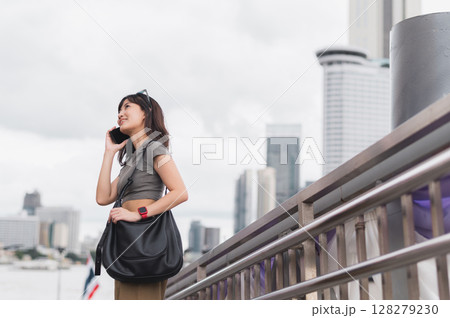 Solo southeast asian woman teenager blogger world travel tourism express joy smartphone wait for friend boat Chao Phraya river Bangkok local cultural experience travel explorer asia concept 128279230