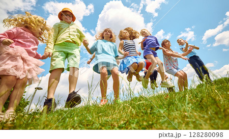 Children jumping in grassy field under summer sky 128280098