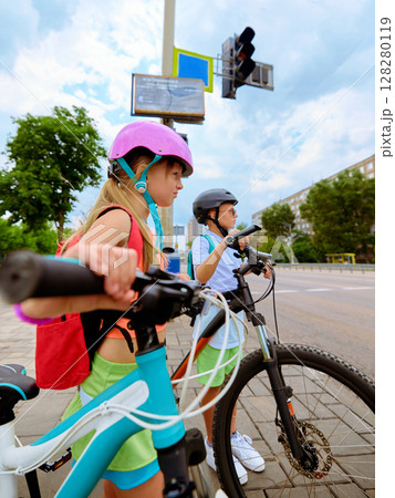 Pause and ride. Two children in helmets waiting to cross at the bike path intersection 128280119