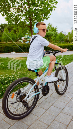 Young boy biking with headphones in sunny park environment Young boy biking with headphones in sunny park environment 128280131