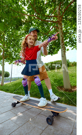 Speed and laughter. Father teaching daughter skateboarding in sunny park 128280258