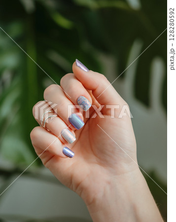 Eye-catching nail art visuals for social media marketing. Skittles nails on hand. Colorful shiny manicure with different textures. Female hand with multicolored nails on green foliage background Eye-catching nail art visuals for social media marketing. Skittles nails on hand. Colorful shiny manicure with different textures. Female hand with multicolored nails on green foliage background 128280592