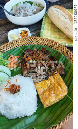 Trung chien or egg omelet, thit heo nuong xa or grilled pork chop and rice on a banana leaf, accompanied by pho bo or beef noodle soup and baguette. Authentic traditional Vietnamese cuisine 128280971