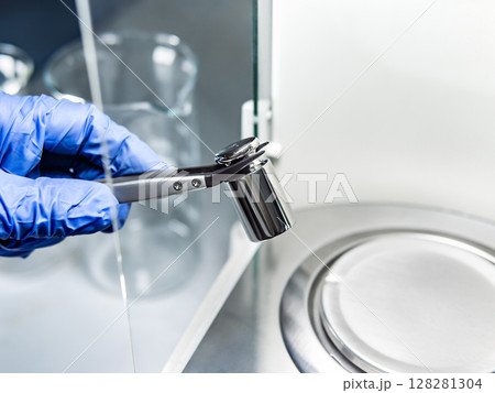 A operator's hand is holding steel calibration weight to place on the analytical balance. A operator's hand is holding steel calibration weight to place on the analytical balance. 128281304