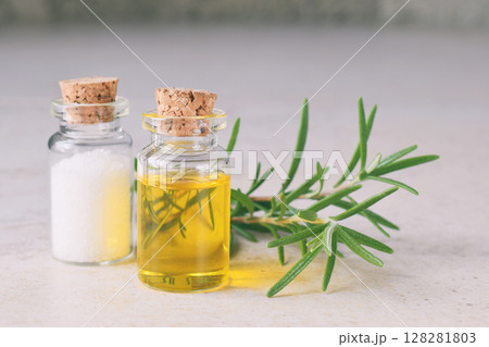 Rosemary essential oil in a small bottle and fresh twig on light background. Natural aroma cosmetic oil and salt Rosemary essential oil in a small bottle and fresh twig on light background. Natural aroma cosmetic oil and salt 128281803