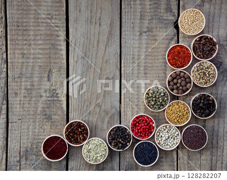 spices on a wooden background. Coriander, black pepper, paprika, mustard, turmeric, cumin, sumac, fenugreek, cloves, cubeb. 128282207