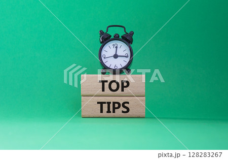 Top Tips symbol. Concept words Top Tips on wooden blocks. Beautiful green background with alarm clock. Business and Top Tips concept. Copy space. 128283267