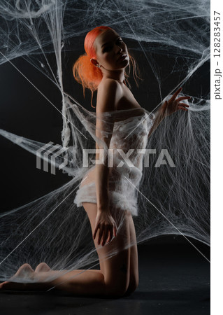 Red-haired woman caught in a delicate web of nets in a dark studio 128283457