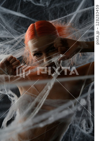 Woman with red hair ensnared in a net amid a web-like trap Woman with red hair ensnared in a net amid a web-like trap 128283459