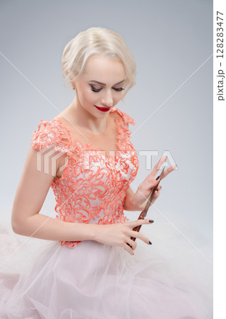 Bride in delicate gown poses with scissors in artistic studio setting Bride in delicate gown poses with scissors in artistic studio setting 128283477