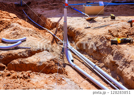 Workers install plumbing pipes in trench at construction site under works day Workers install plumbing pipes in trench at construction site under works day 128283851