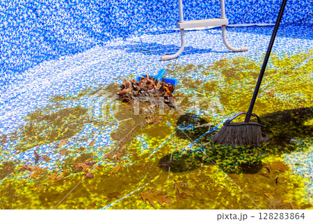 Manual labor is being done to remove leaves muck from stagnant swimming pool on works day. 128283864