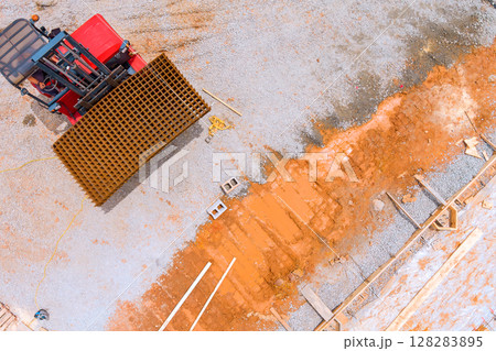 Heavy machinery operates at construction site, moving metal mesh preparing foundation during works day hours. 128283895