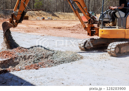 An excavator moves gravel on construction site with works day 128283900