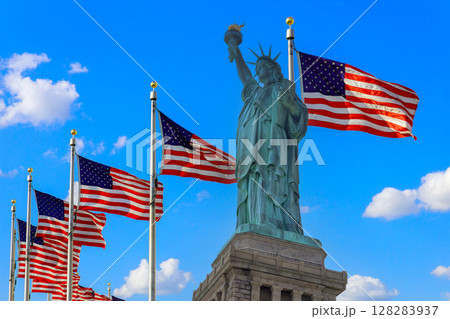 Statue of Liberty displays her torch proudly while several American flags wave nearby against bright sky. Statue of Liberty displays her torch proudly while several American flags wave nearby against bright sky. 128283937