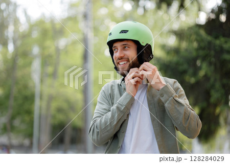 Man smiles while adjusting green helmet outdoors in a park setting before cycling or skating Man smiles while adjusting green helmet outdoors in a park setting before cycling or skating 128284029