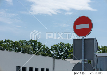 A bright red do not enter sign stands prominently in front of modern buildings under a blue sky, conveying a clear road instruction A bright red do not enter sign stands prominently in front of modern buildings under a blue sky, conveying a clear road instruction 128284088