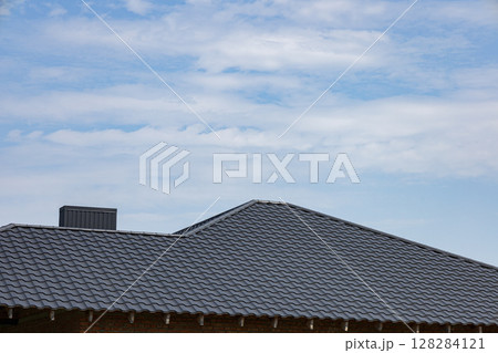 Metallic roofing features a sleek tiled design, reflecting sunlight under a clear blue sky at a construction site during daylight hours 128284121