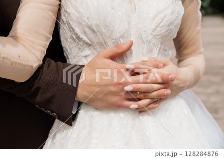 Intimate Wedding Moment: Couple Embracing with Focused Hands Holding Wedding Rings, Luxurious Dress, Brown Suit, Sparkling Texture. Intimate Wedding Moment: Couple Embracing with Focused Hands Holding Wedding Rings, Luxurious Dress, Brown Suit, Sparkling Texture. 128284876