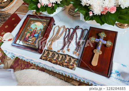 Orthodox Religious Ceremony Setup with Icon, Rosaries, Cross, and Floral Arrangements on Table with Lace Orthodox Religious Ceremony Setup with Icon, Rosaries, Cross, and Floral Arrangements on Table with Lace 128284885
