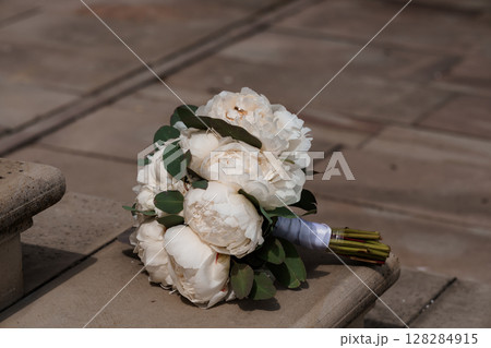 Elegant Wedding Bouquet of White Peonies and Eucalyptus on a Stone Bench: A Romantic Floral Arrangement for Celebration 128284915