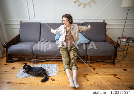Yawning apathetic woman stretching in relaxed pose while cat lying on floor, boredom and laziness 128285554
