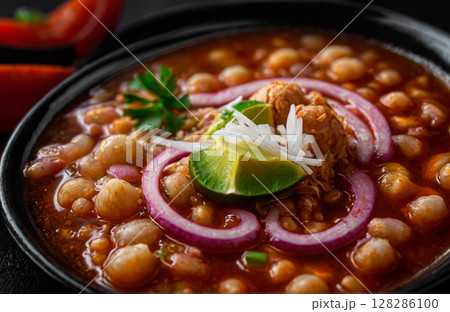 Traditional slow cooked Mexican pozole rojo soup with ground minced beef, hominy maiz and dry ancho paprika in cast-iron roasting dish on old rustic wooden board 128286100