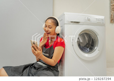 A Joyful Moment in the Laundry Room A Woman Laughing While Using Her Smartphone 128287294