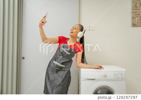 Cheerful Young Woman Happily Taking a Selfie in a Bright Modern Laundry Room 128287297