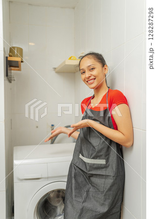 A Happy Smiling Woman Showcasing a Washing Machine in a Modern Laundry Room A Happy Smiling Woman Showcasing a Washing Machine in a Modern Laundry Room 128287298