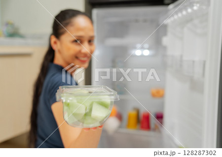 Healthy Snack Choices: Woman Holding Fresh Melon Cubes Near Open Refrigerator 128287302
