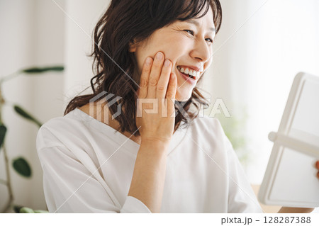 鏡で肌を見て笑顔になる50代のミドル女性 128287388