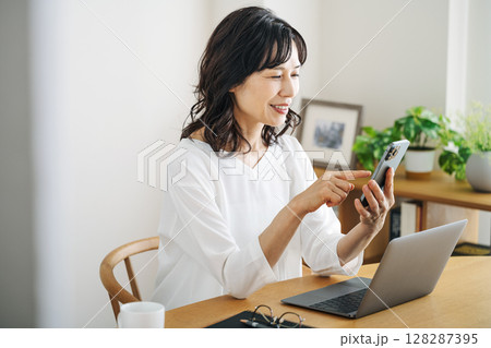 家のリビングでスマホを見る50代のミドル女性 128287395