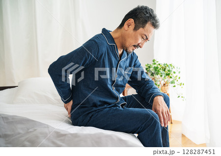 ベッドの上で腰痛に悩む50代の男性 128287451
