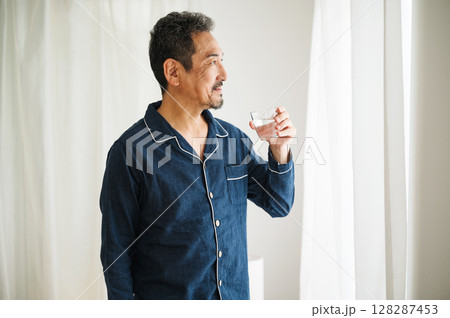 朝パジャマ姿で寝起きにコップ一杯の水を飲む50代のミドル男性 128287453