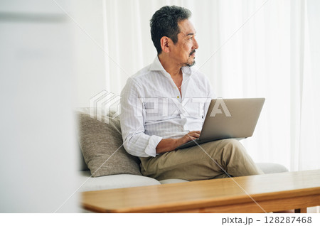 リビングのソファーでパソコン作業をする50代のミドル男性 128287468