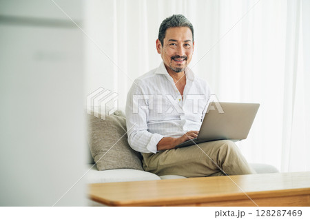 リビングのソファーでパソコン作業をする50代のミドル男性 128287469