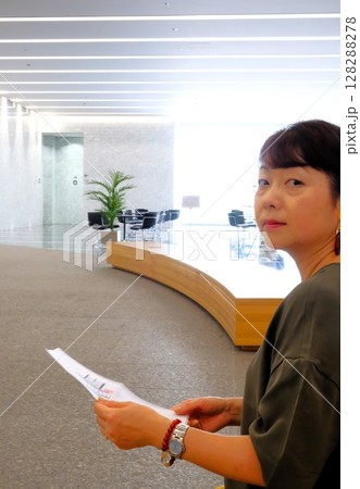 自然光の入る明るいオフィスで書類を手にしたまま振り返る女性 自然光の入る明るいオフィスで書類を手にしたまま振り返る女性 128288278