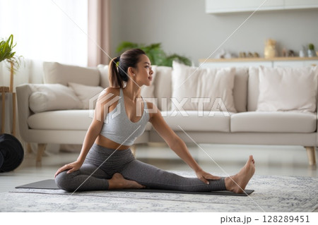 Young woman doing yoga stretches in the living room at home Young woman doing yoga stretches in the living room at home 128289451