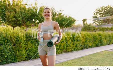 A Vibrant Active Young Woman Is Holding a Yoga Mat and Water Bottle While Enjoying the Outdoors A Vibrant Active Young Woman Is Holding a Yoga Mat and Water Bottle While Enjoying the Outdoors 128290075