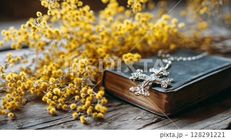 Cross of Jesus Christ resting on a holy bible surrounded by beautiful yellow flowers, evoking prayer and worship in serene setting 128291221