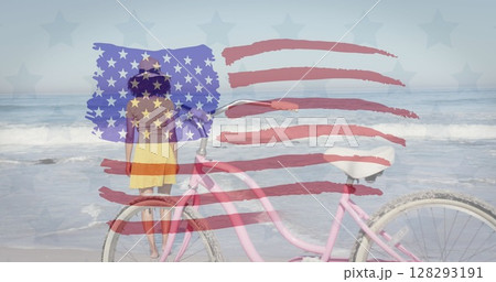 American flag waving against rear view of african america woman with bicycle standing at the beach 128293191