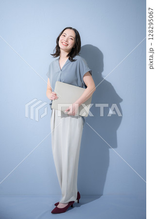水色背景でパソコンを持つ爽やかな春夏の半袖ビジネス(オフィスカジュアル)の女性 転職や人事 水色背景でパソコンを持つ爽やかな春夏の半袖ビジネス(オフィスカジュアル)の女性 転職や人事 128295067